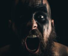 A shaven headed Viking with a beard with black warpaint screams