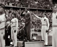 Jesse Owens salutes while standing on top of the podium after winning gold in the long jump at the 1936 Olympics. Luz Long (R) stands in the second position while giving the Nazi salute.
